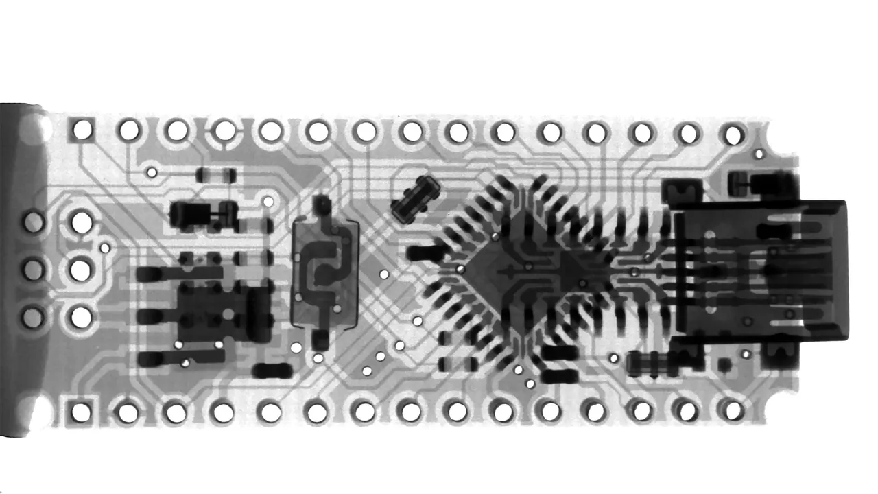 Radiografia di una piccola scheda a microcontrollore con le piste, un chip e una presa USB sul bordo