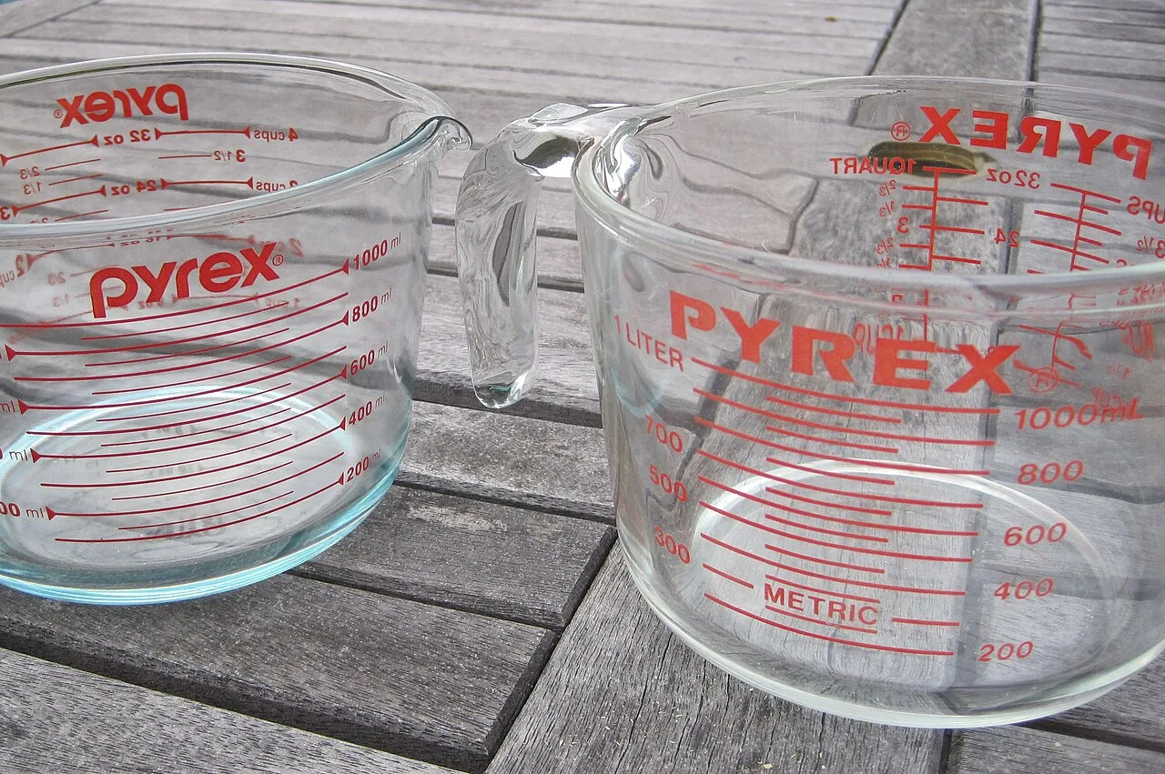 Two glass measuring jugs with red graduations in cups, ounces and millilitres