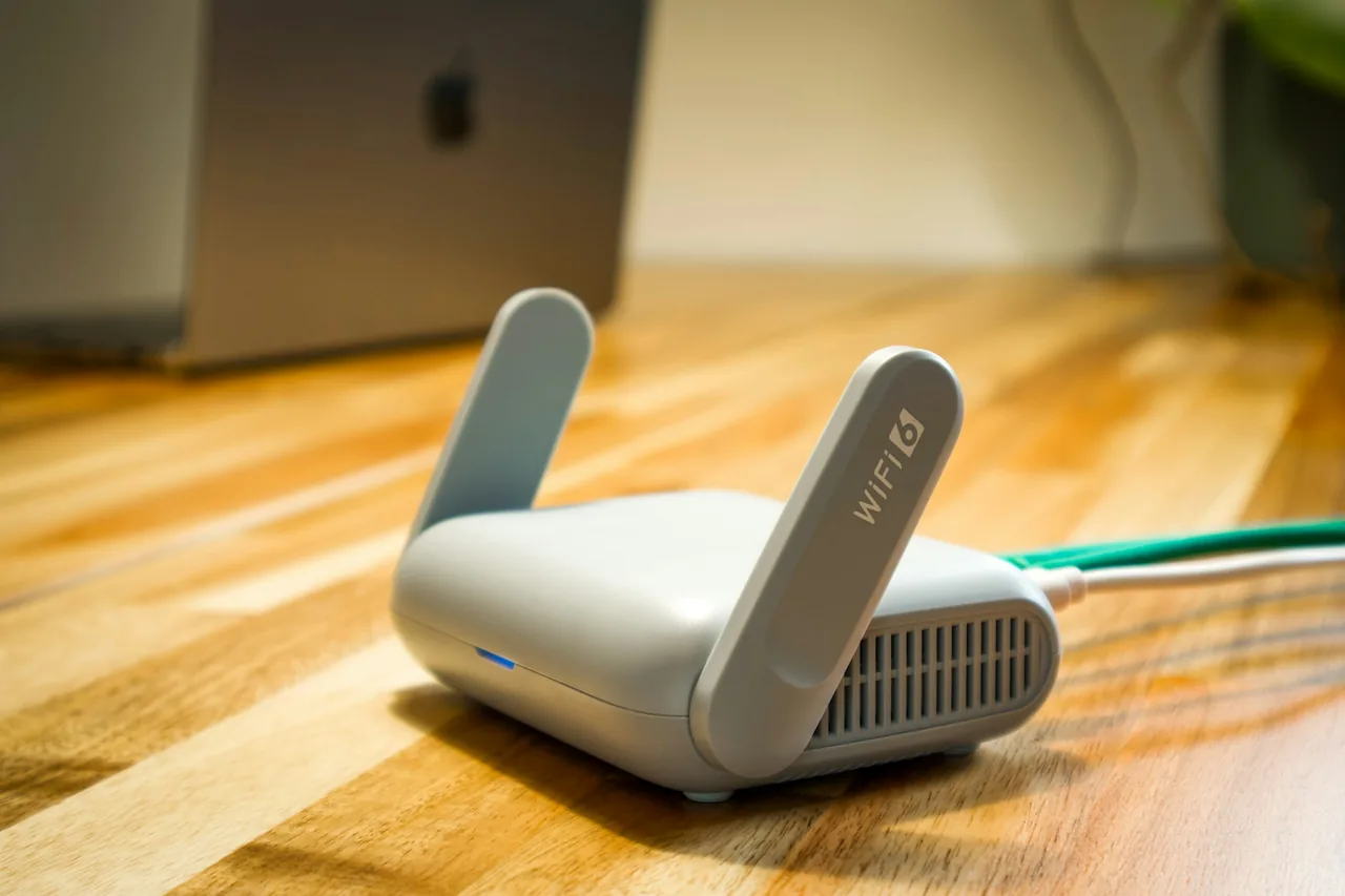Mały szary router z dwiema antenami, na jednej z nich napis WiFi 6, w tle laptop