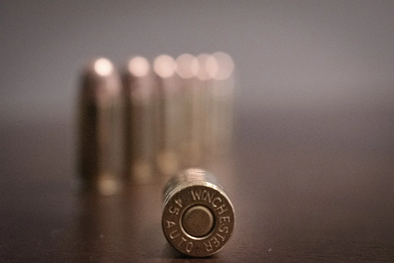 Denko łuski z wybitym napisem WINCHESTER 45 AUTO, za nim rozmyty rząd nabojów