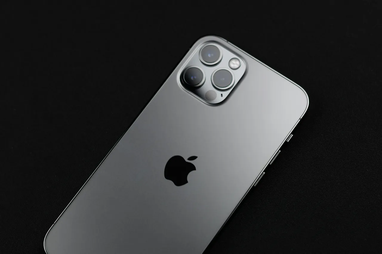 Tył grafitowego iPhone’a z trzema obiektywami aparatu na czarnym tle