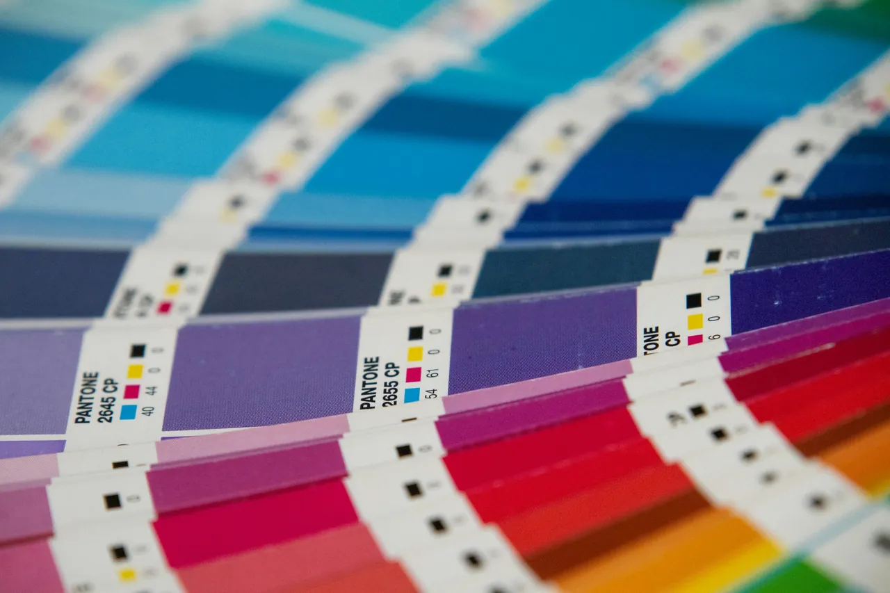 Rozłożony wzornik Pantone z fioletowymi i czerwonymi próbkami oraz etykietami z czterema liczbami przy kwadracikach w kolorach farb