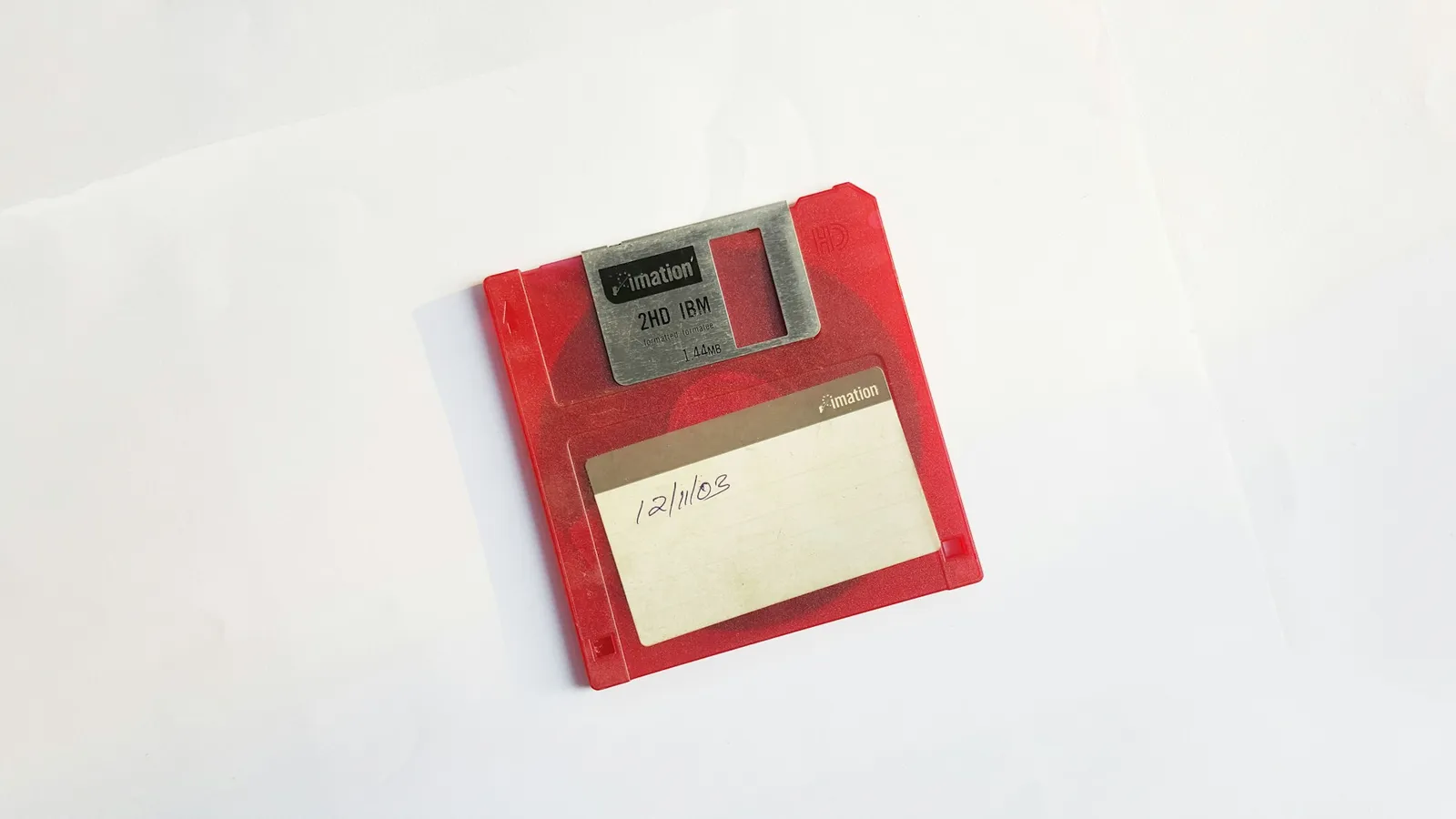 Czerwona dyskietka 3,5 cala firmy Imation z napisem 2HD IBM i 1.44MB na metalowej osłonie oraz ręcznie wpisaną datą na etykiecie
