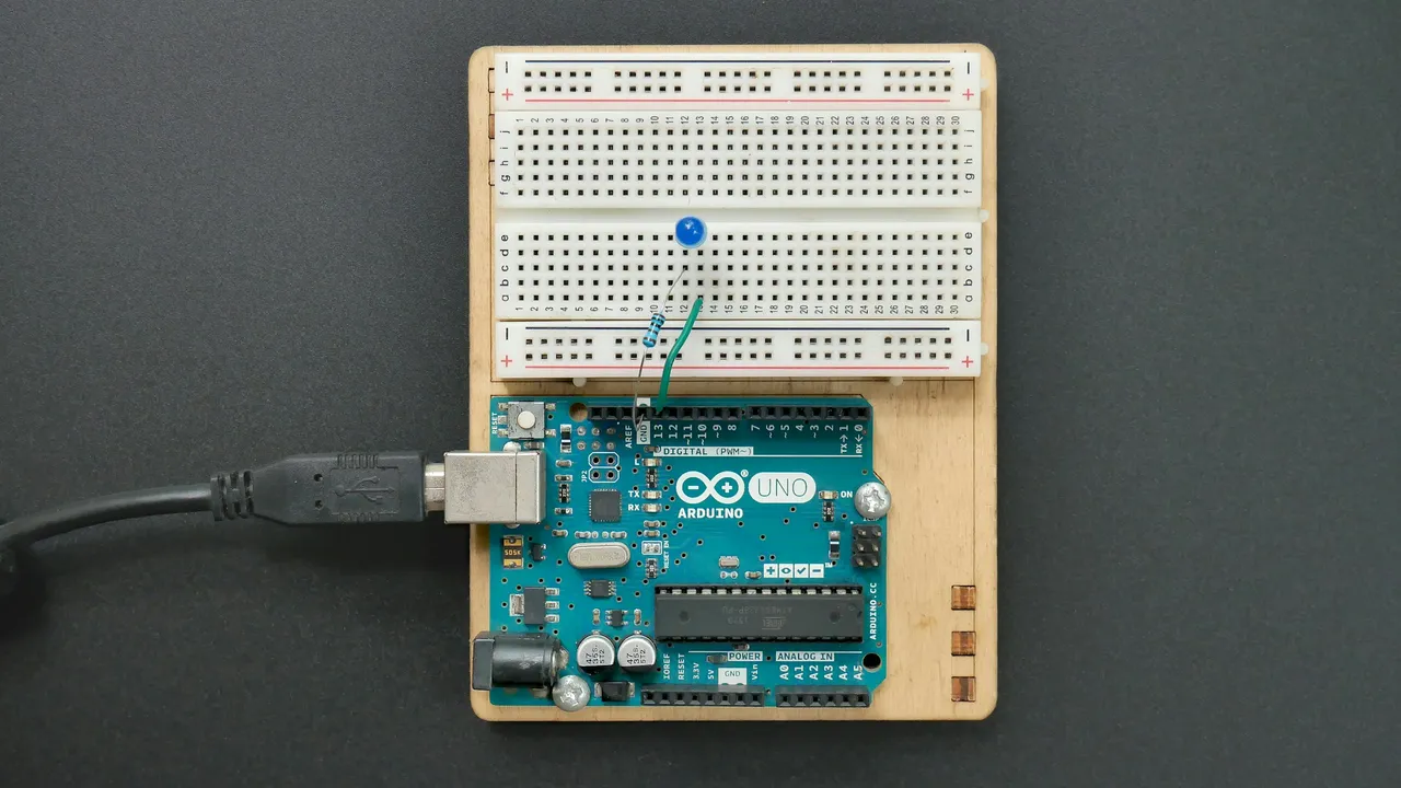 Scheda Arduino Uno con un cavo USB collegato e, sopra, una breadboard con un LED blu e una resistenza