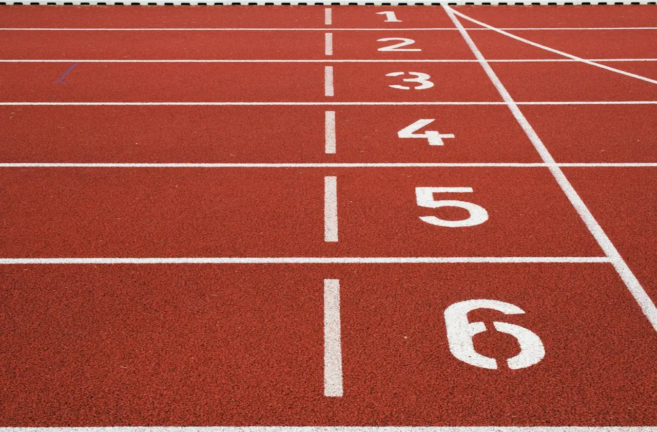 Czerwona bieżnia lekkoatletyczna z białymi liniami torów i numerami od jednego do sześciu przy linii startu