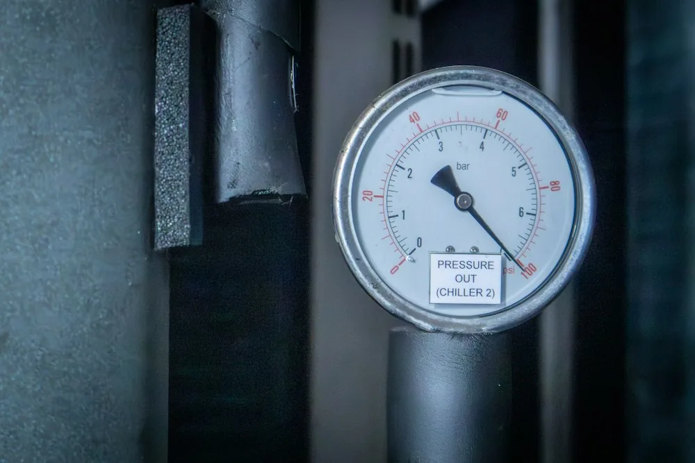 Manometr na czarnej rurze, z czarną skalą w barach i czerwoną skalą w psi, z tabliczką PRESSURE OUT