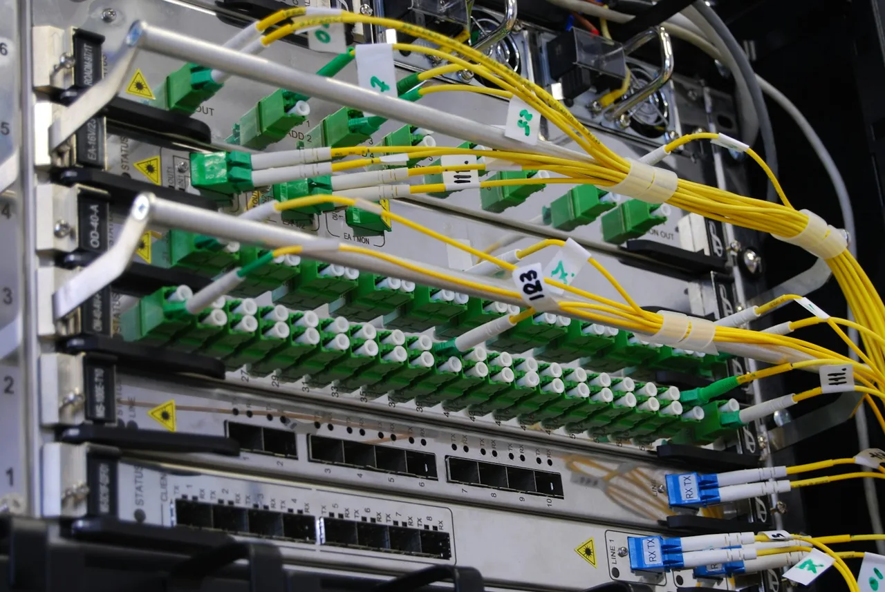 Żółte przewody światłowodowe wpięte w zielone gniazda modułów w szafie telekomunikacyjnej, obok niebieskie wtyki z oznaczeniami RX i TX