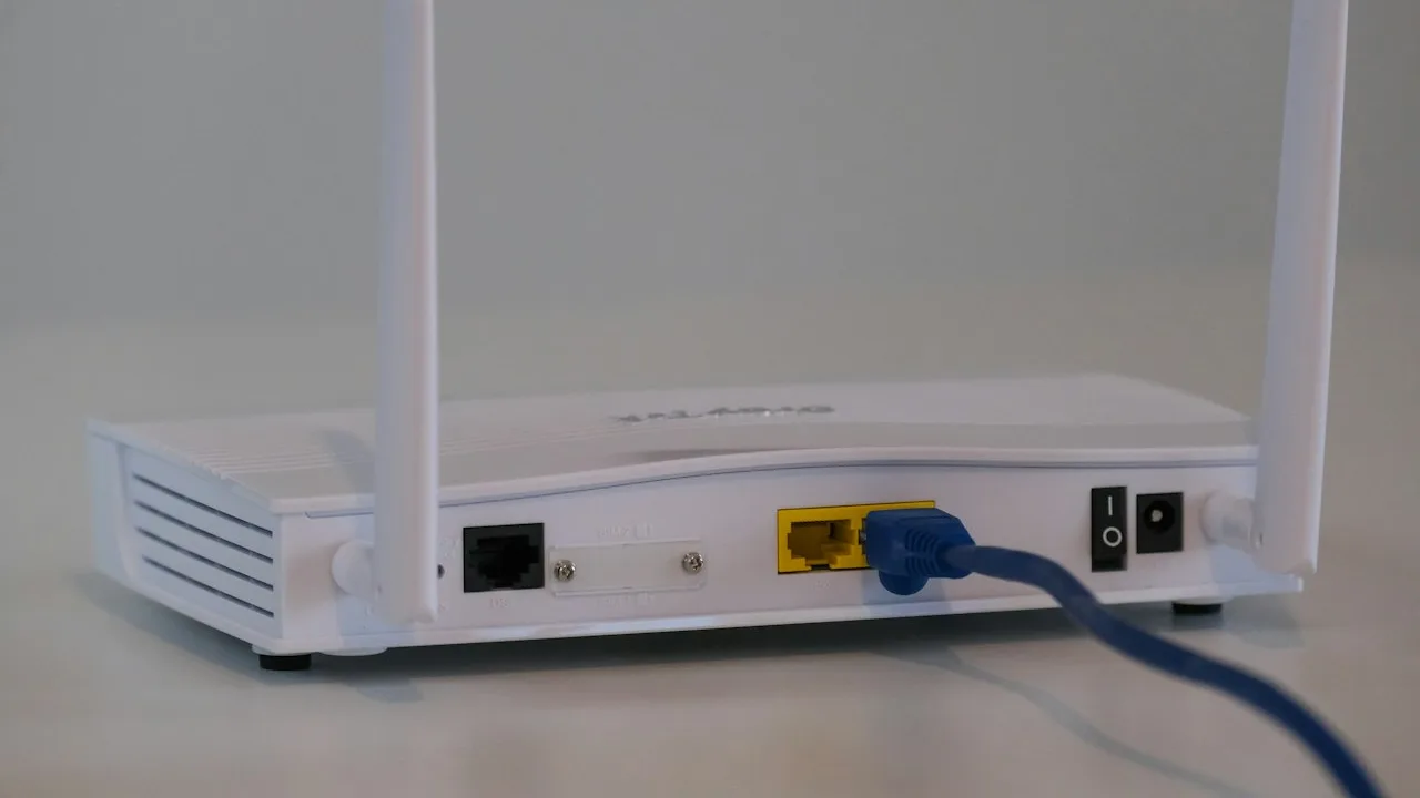 Router z dwiema antenami, widziany od tyłu, z niebieskim przewodem w żółtym gnieździe