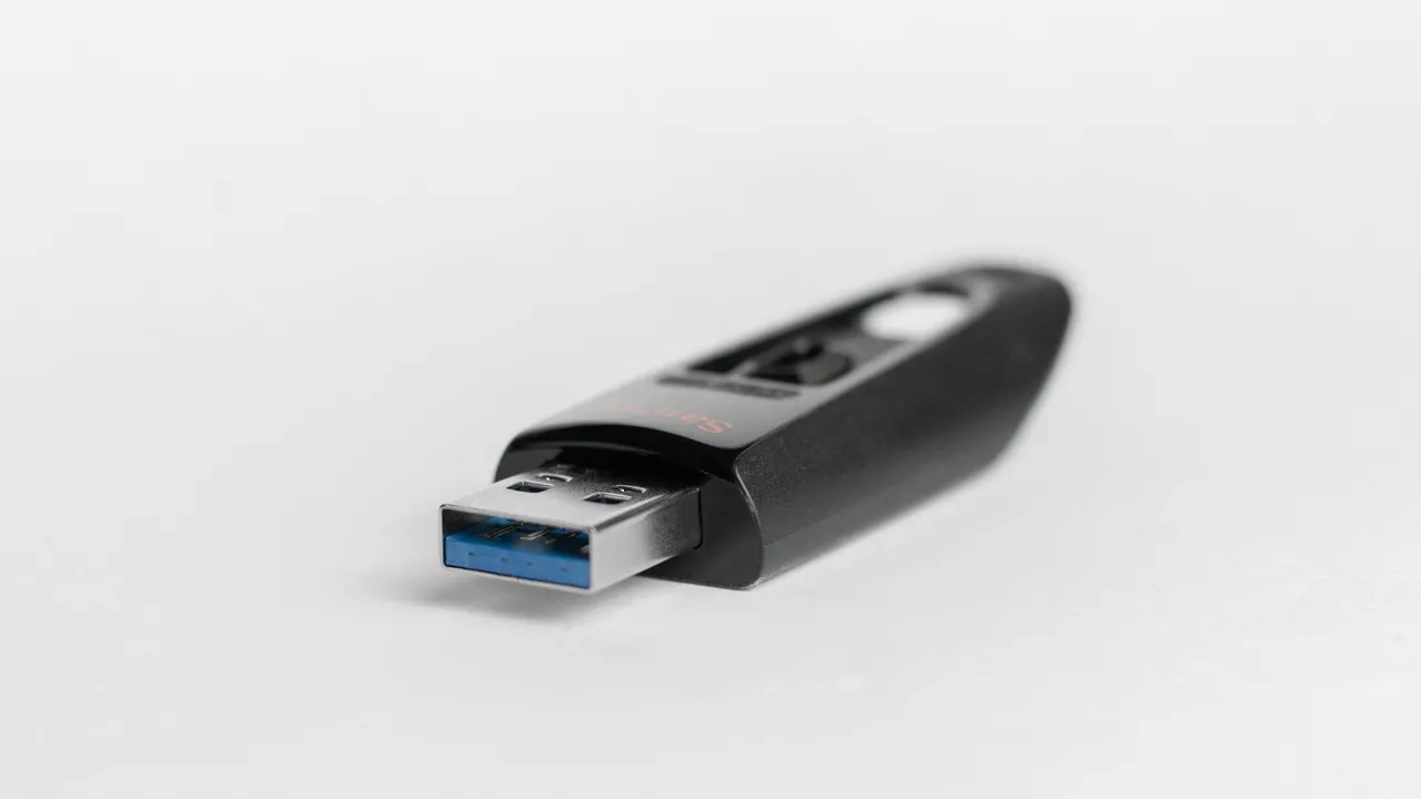 Czarny pendrive z wysuniętą wtyczką USB-A z niebieską wkładką na białym tle