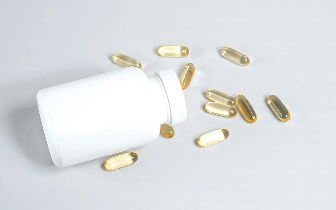 A white supplement bottle on its side with amber softgel capsules spilled around it