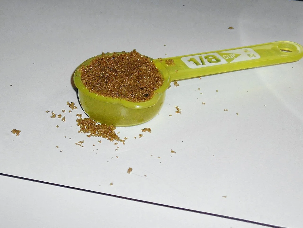 A one-eighth cup measure filled with sugar, marked 1/8 cup and 30 ml