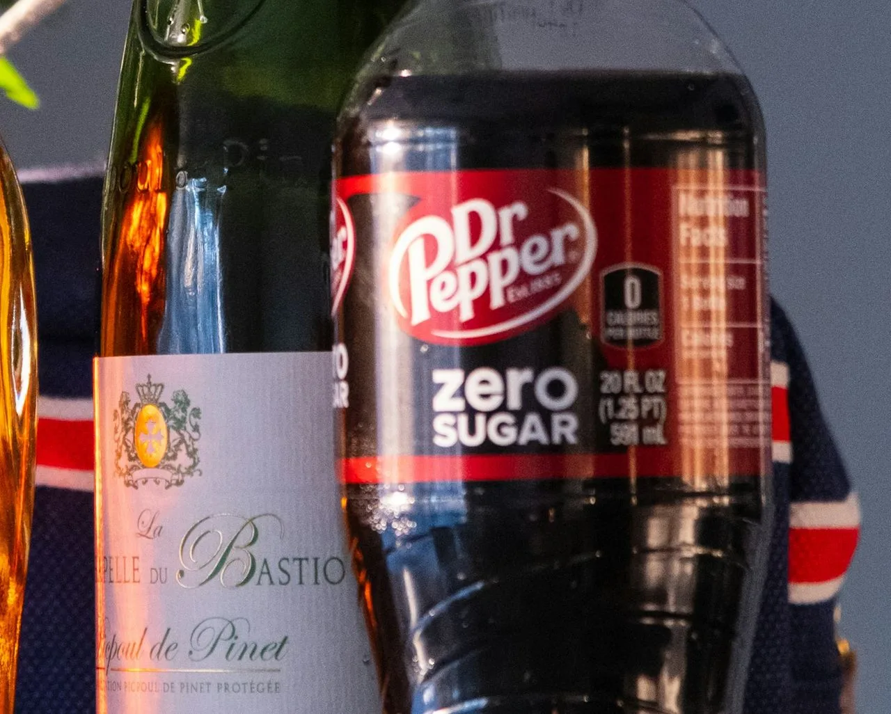 Plastikowa butelka napoju z napisem 20 FL OZ (1.25 PT) 591 mL na etykiecie, stojąca obok butelki wina