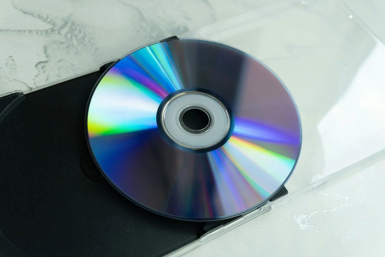 Płyta DVD-R z wielobarwnymi odbiciami światła leżąca w otwartym plastikowym pudełku