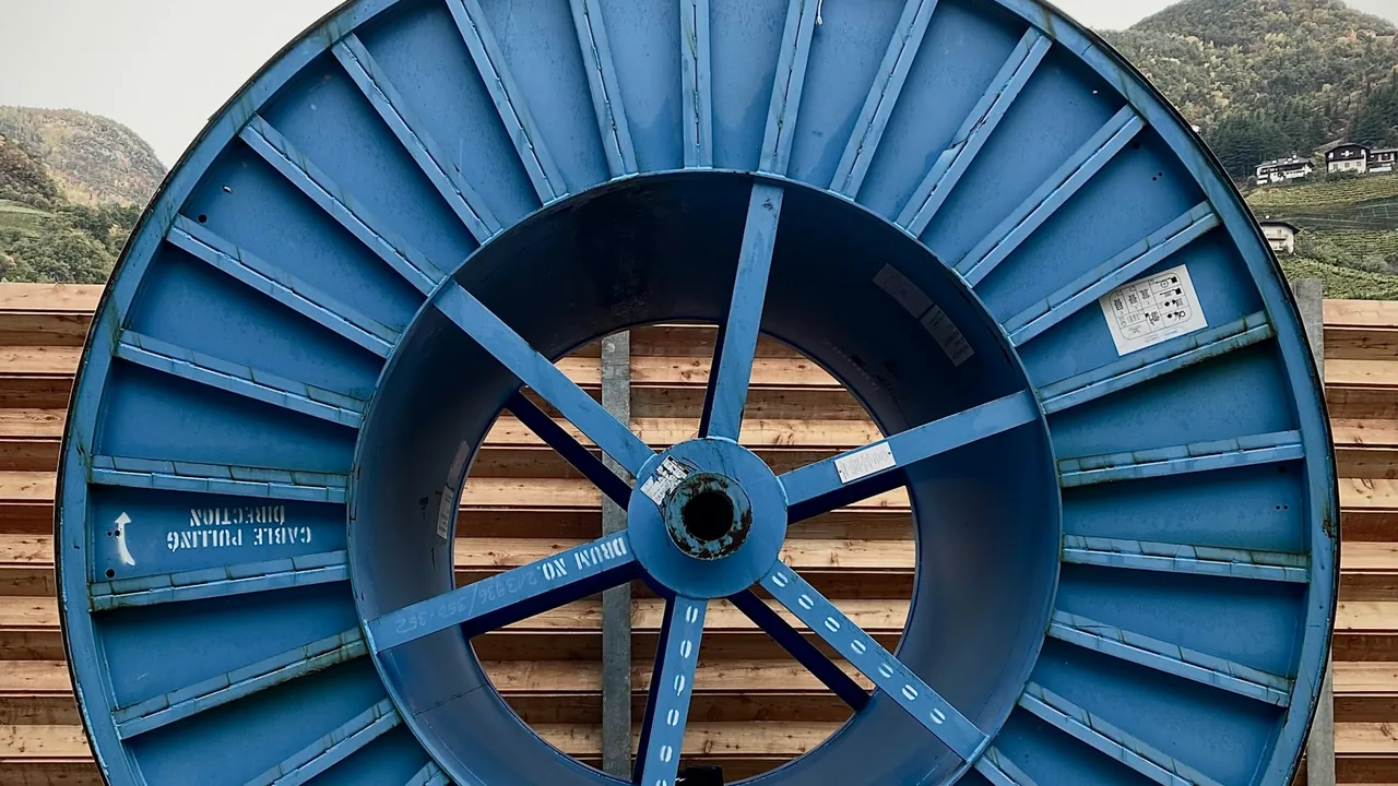 A blue cable drum in front of a wooden wall, with an arrow and the words Cable pulling direction