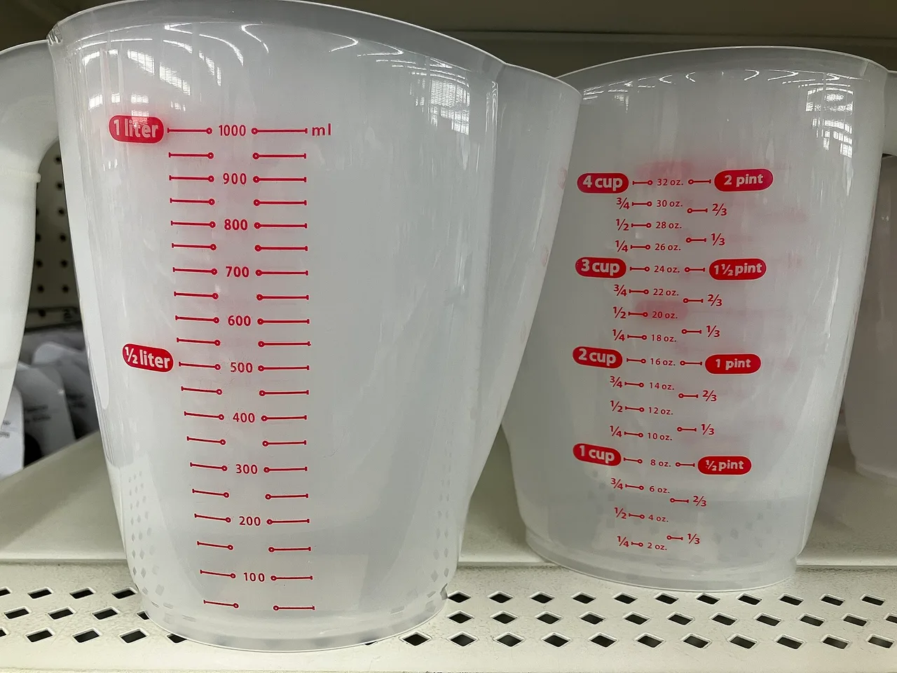 Two plastic kitchen measuring jugs: the left one graduated in millilitres, the right one in cups, ounces and pints