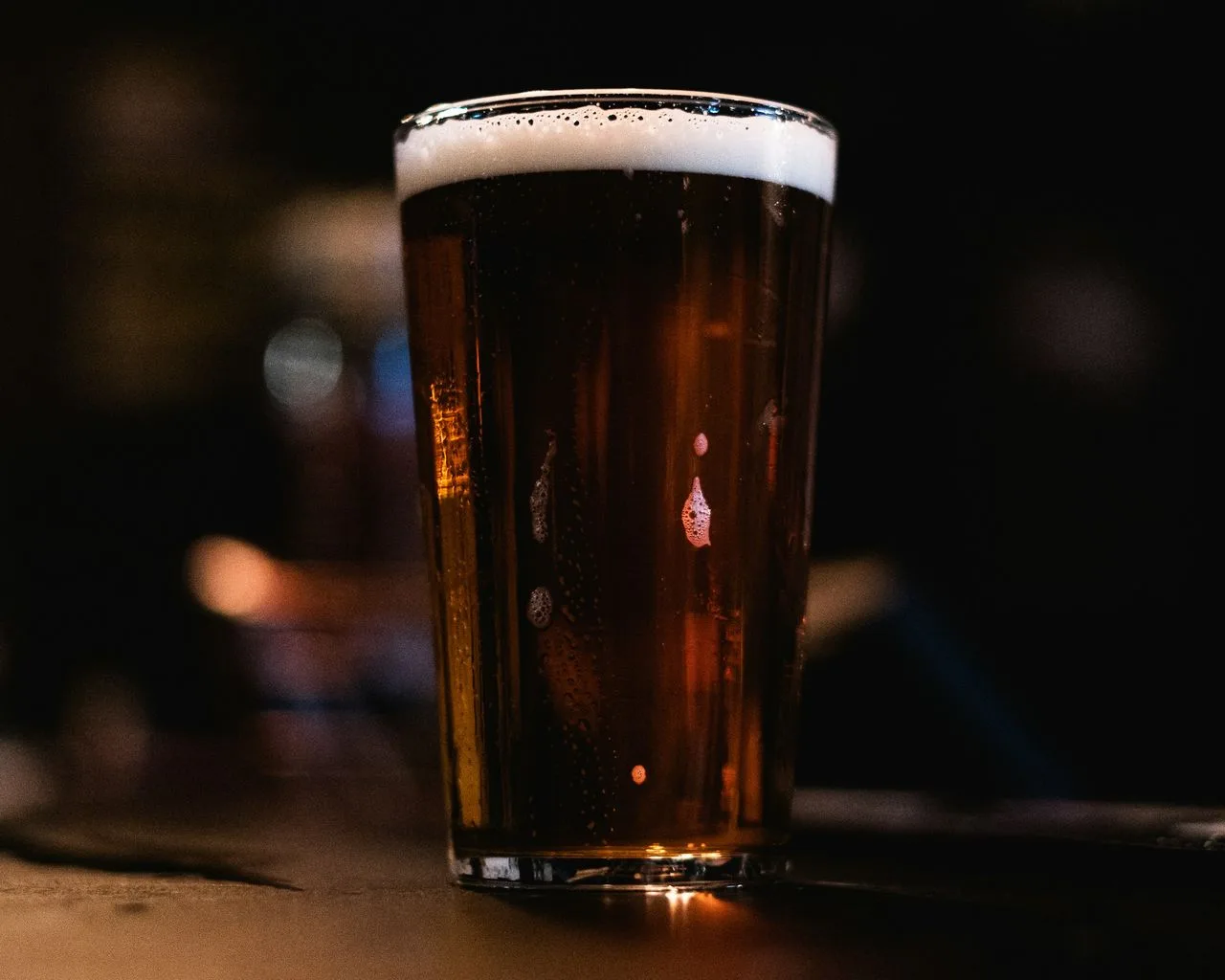 Stożkowa szklanka piwa z białą pianą, stojąca na barze w ciemnym wnętrzu