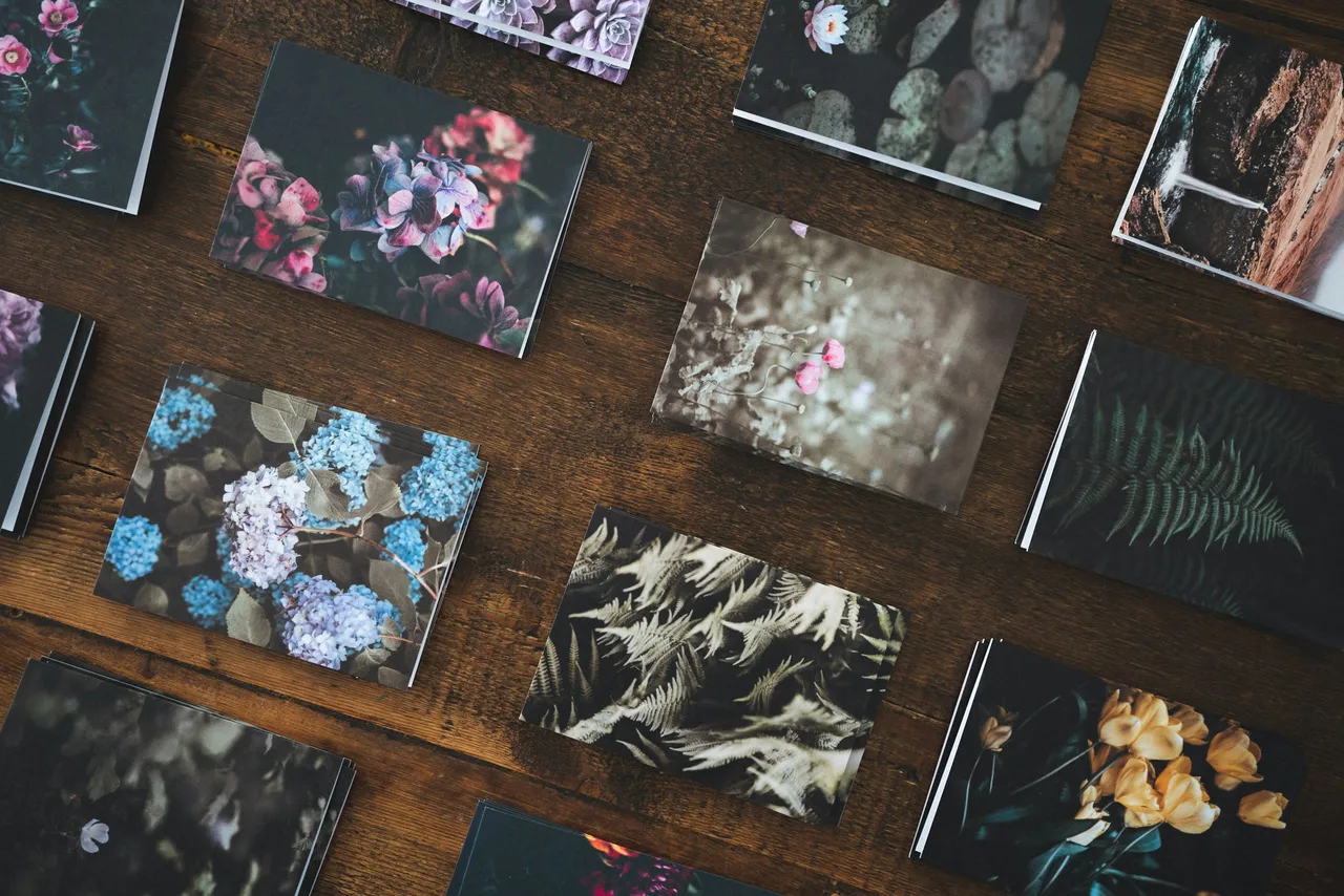 Pile di cartoncini stampati con foto di fiori e felci su un tavolo di legno