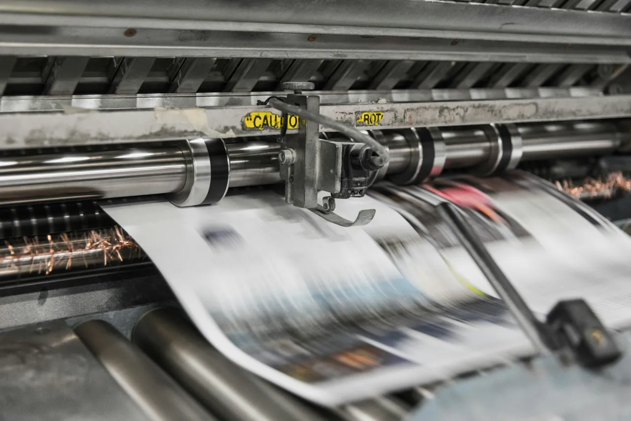Zadrukowany papier przesuwa się między metalowymi walcami maszyny drukarskiej