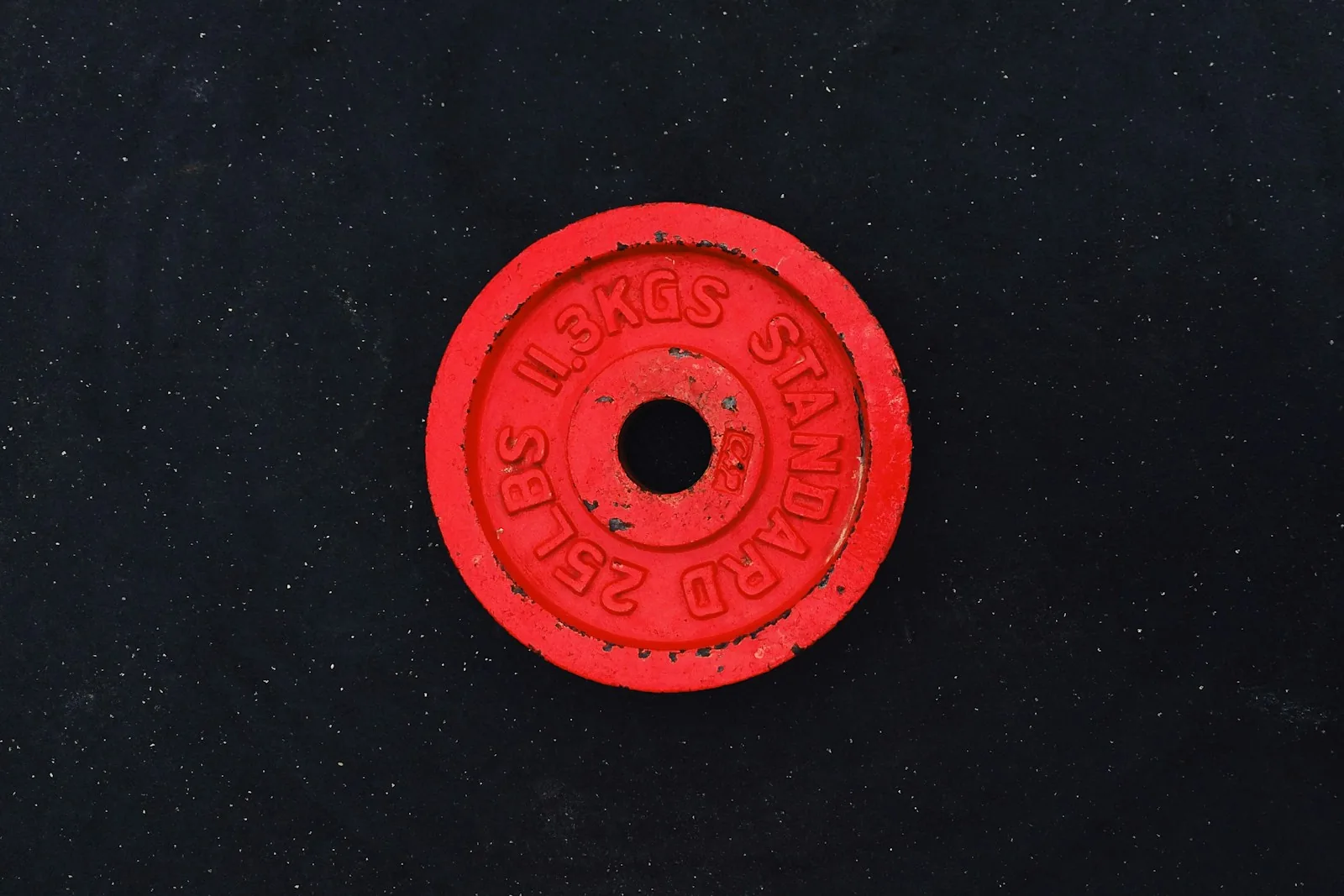 A red barbell plate cast with the wording 25 LBS and 11.3 KGS