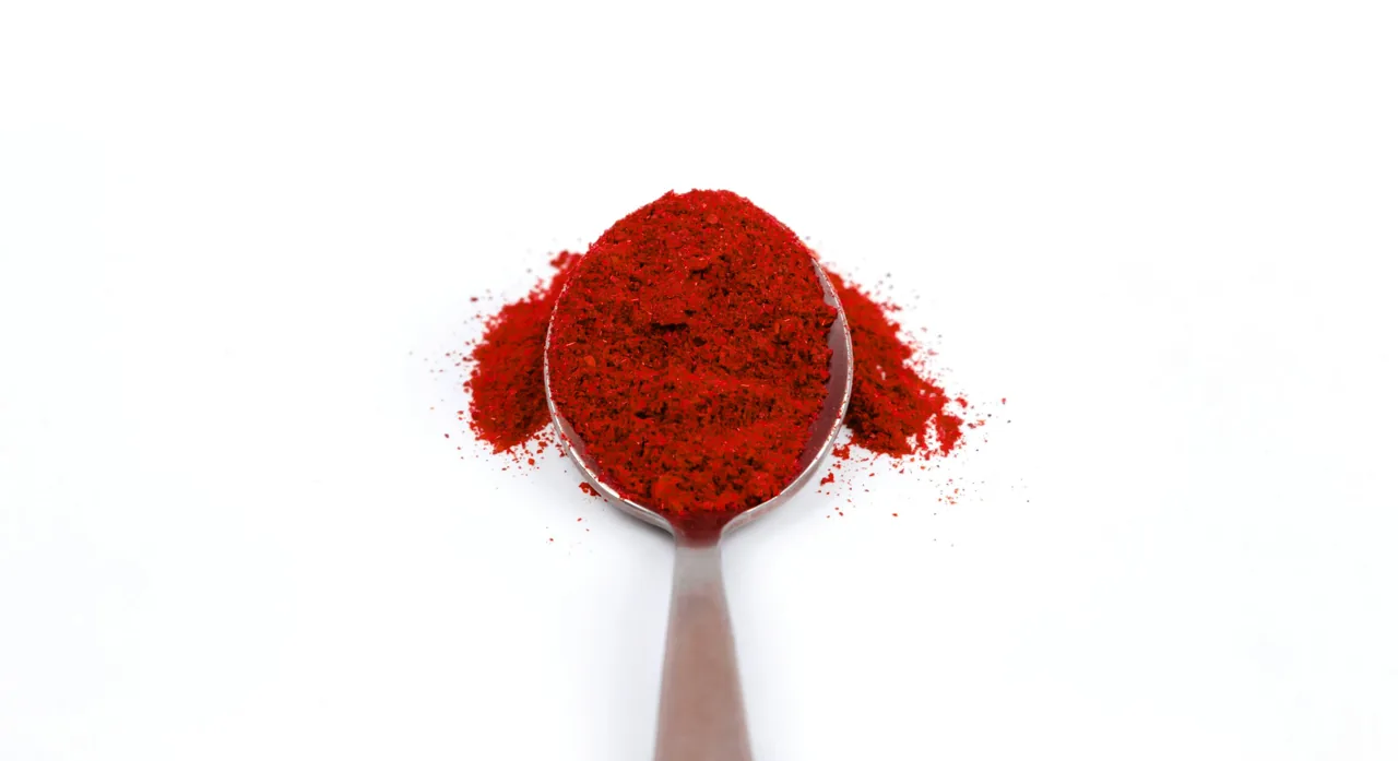 Metalowa łyżka z czubatą porcją mielonej papryki chili na białym tle