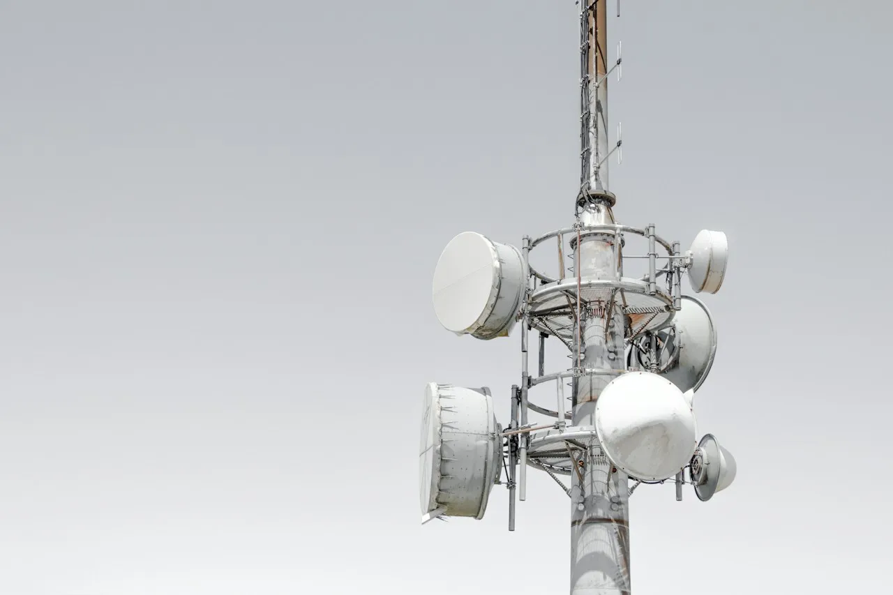 Maszt telekomunikacyjny z okrągłymi antenami pod białymi osłonami na tle jasnoszarego nieba