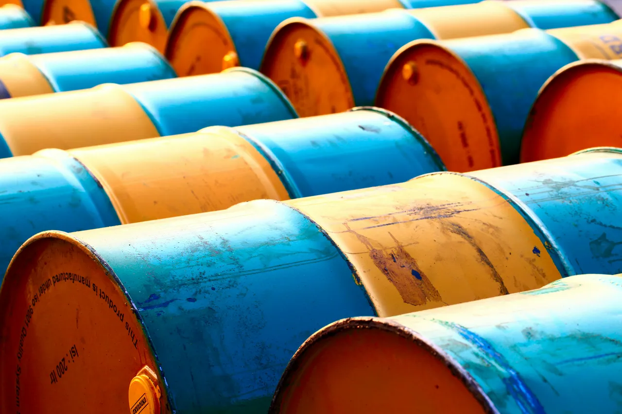 Metalowe beczki ułożone w rzędach, na pomarańczowym denku najbliższej napis Isi : 200 ltr