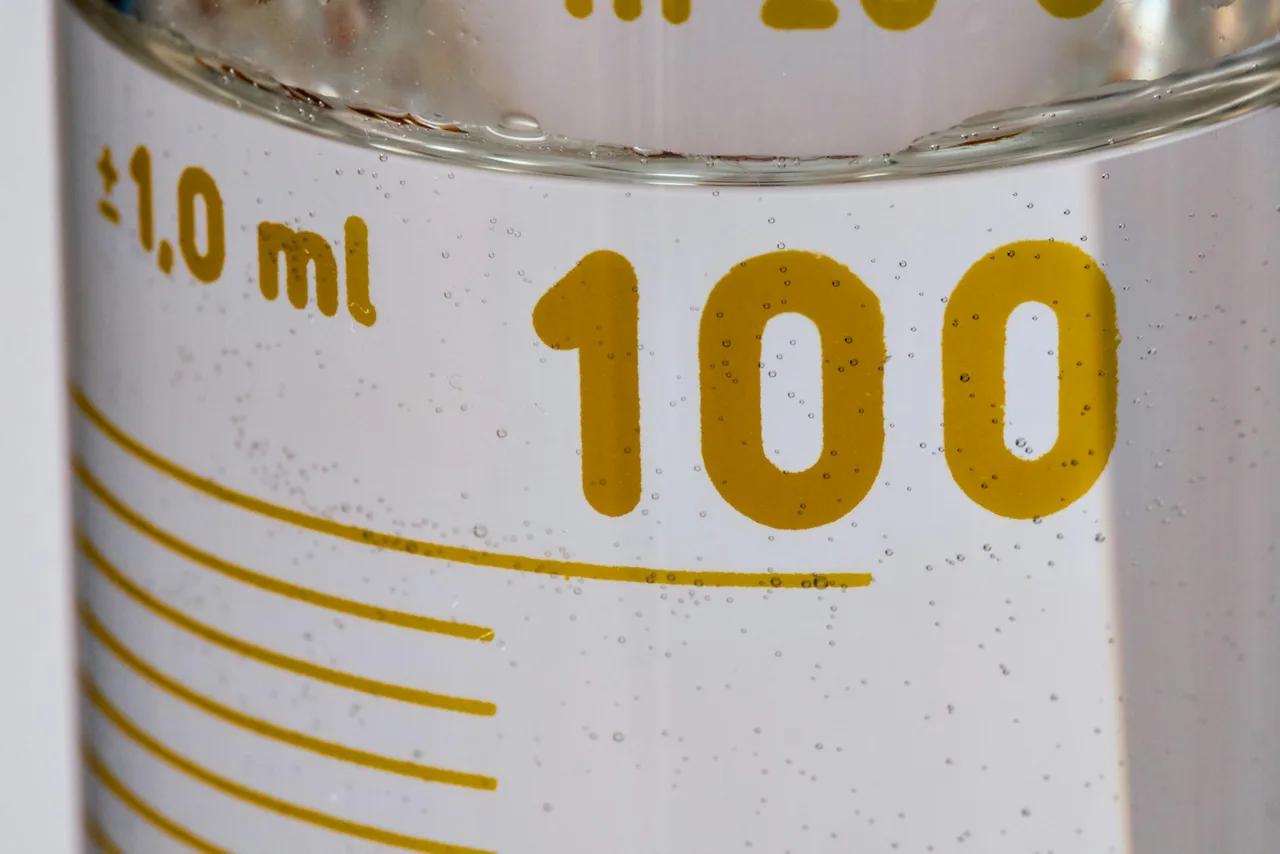 Zbliżenie na cylinder miarowy z żółtą kreską i liczbą 100 oraz napisem plus minus 1,0 ml