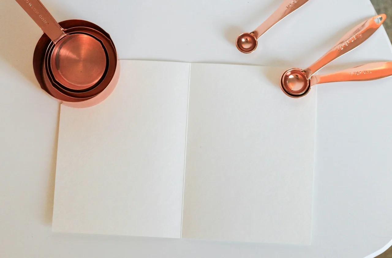 Copper-coloured measuring cups nested one inside another and measuring spoons beside a folded white sheet