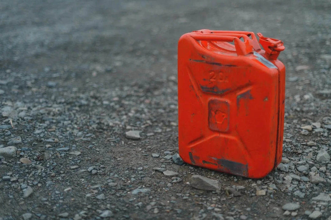 Una tanica di acciaio rossa per carburante con la scritta in rilievo 20 L, appoggiata sulla ghiaia